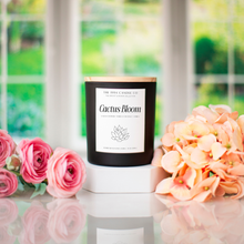 Load image into Gallery viewer, Matte Black Candle labeled 'Cactus Bloom' with pink and peach flowers on a reflective surface.