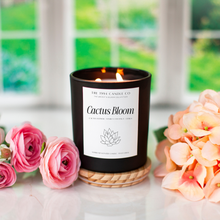 Load image into Gallery viewer, Matte black burning candle labeled 'Cactus Bloom' with peach and pink flowers on a table.
